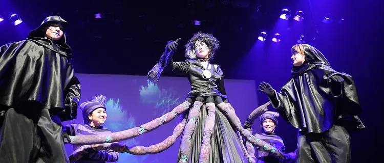 Student in an octopus costume with performers holding its tentacles on stage