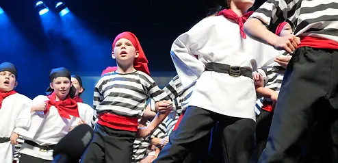Performers in pirate costumes with red sashes singing on stage under blue spotlights