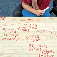 Student leaning over a desk covered in handwritten multiplication problems and red counters