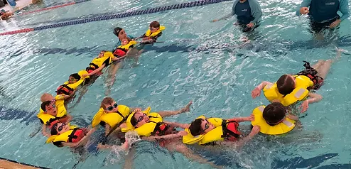 Students in yellow life jackets linked together in a chain during a swimming program lesson