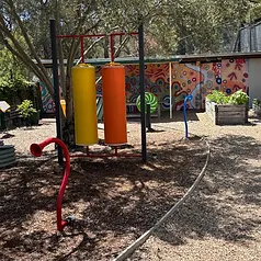 Musical and sensory playground instruments beside an Indigenous dot painting mural