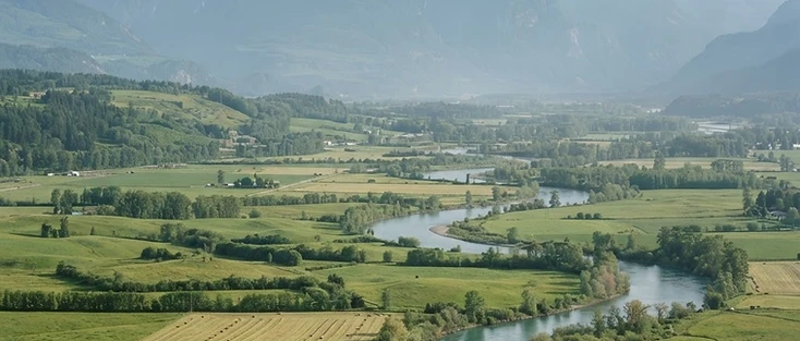 A view of rolling farmland and a river valley with mountains beyond in the Fraser Valley region of British Columbia, where Cassin is located.