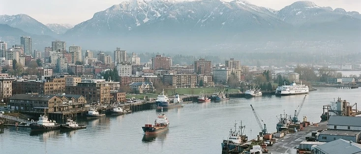 A view of a calm waterfront city with coastal mountains beyond in the Metro Vancouver region of British Columbia, where Ioco is located.