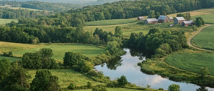 A view of rolling green countryside with a calm river in the Eastern Ontario region of Ontario, where Loyalist is located.