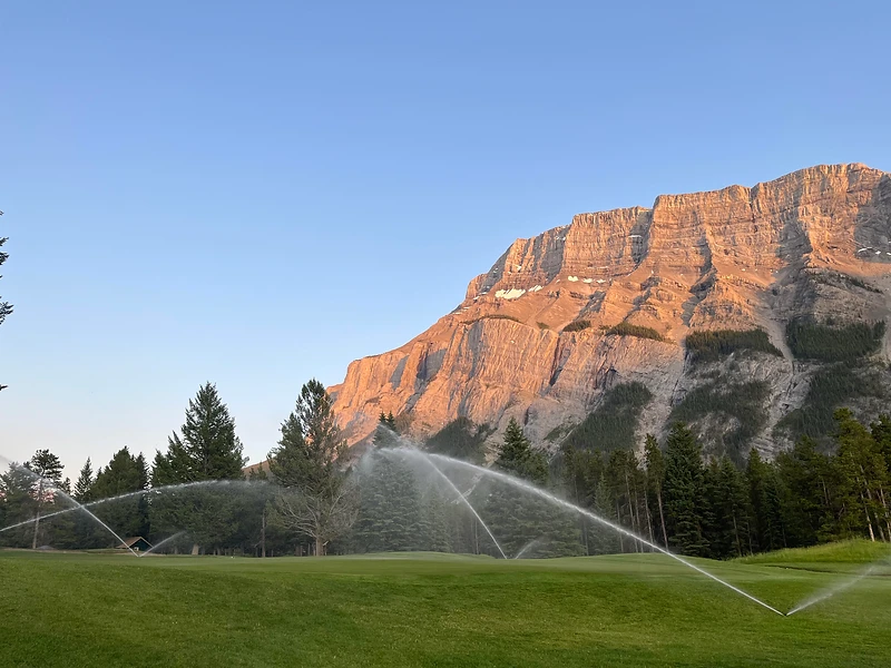 GreenUp irrigation sprinklers on a golf green beneath a lit mountain face