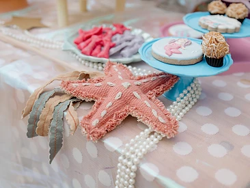 Mesa de festa com tema marinho: estrela-do-mar de tecido, pérolas e biscoitos de sereia