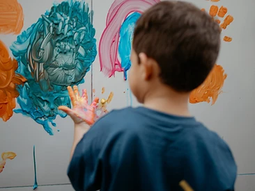 Criança pintando na parede com as mãos em cores vibrantes