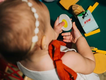 Criança brincando com comida de madeira na mesinha verde