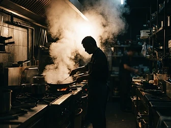 Steam rising in a dark professional kitchen with a silhouetted chef