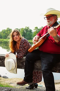 Faye and Corey resting on a rail by the water with a guitar