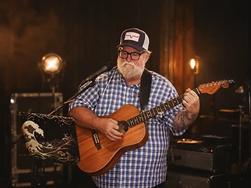 Corey playing acoustic guitar on a warmly lit stage