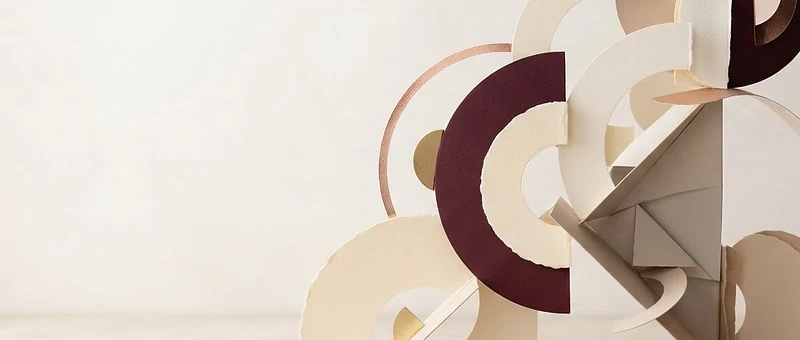 Editorial still-life of layered, intersecting cardstock forms in burgundy, cream, and rose-gold — an artistic representation of ideas coming together