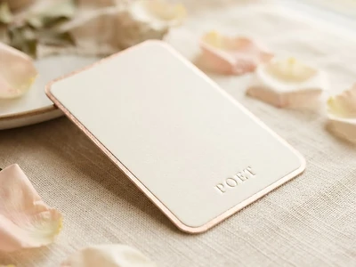 A premium ivory card with a rose-gold edge and POET monogram resting on cream linen