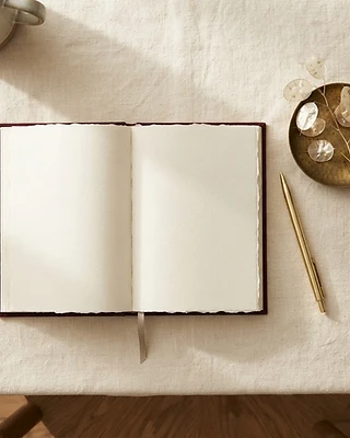 An open burgundy journal resting on warm linen