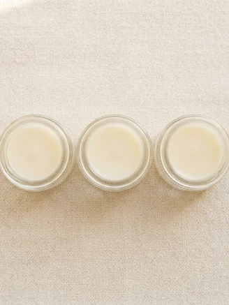 Three small clear sample pots of ivory solid perfume presented together on neutral linen