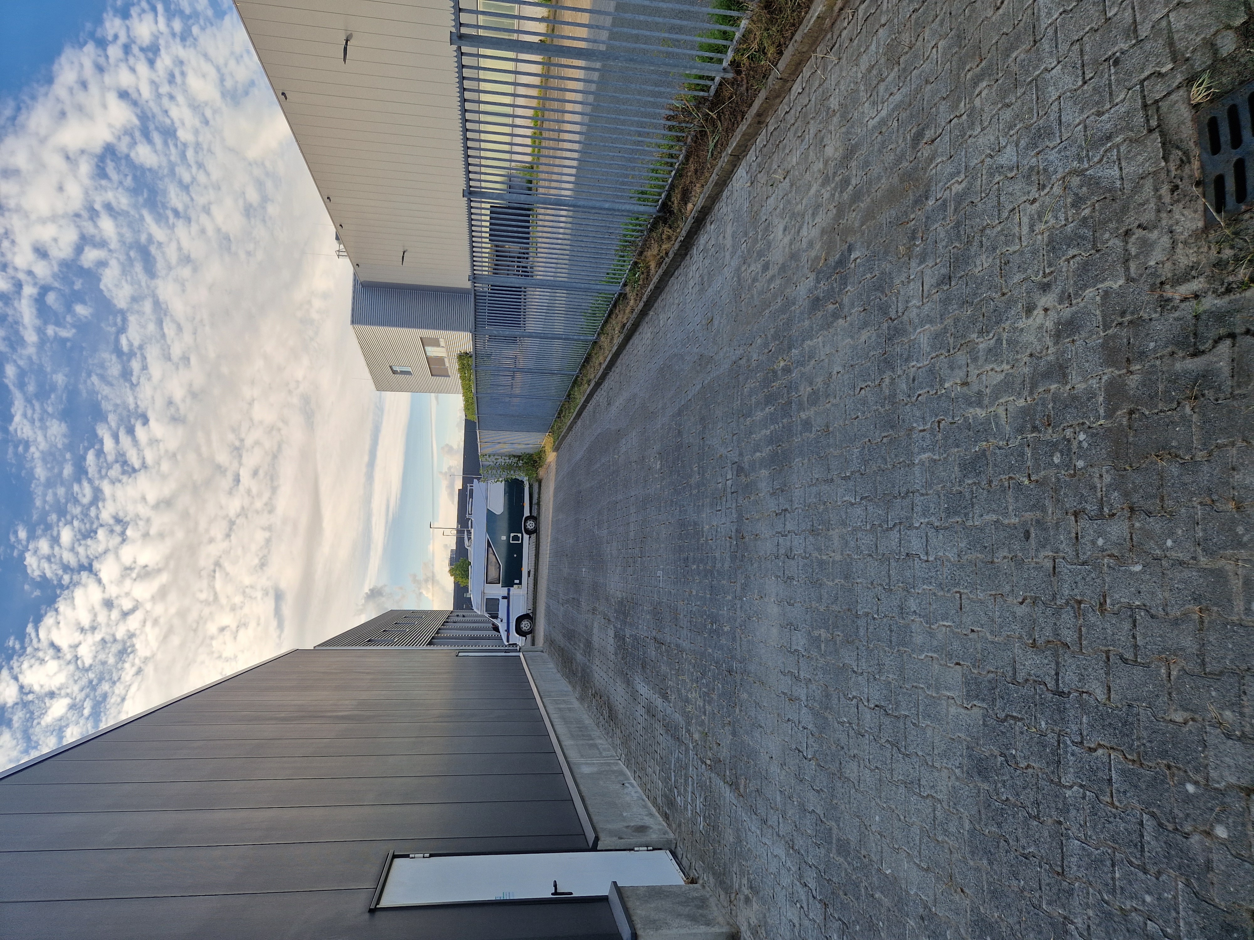 Bestraat pad langs een bedrijfspand en metalen hekwerk, onderdeel van bedrijventerreinonderhoud