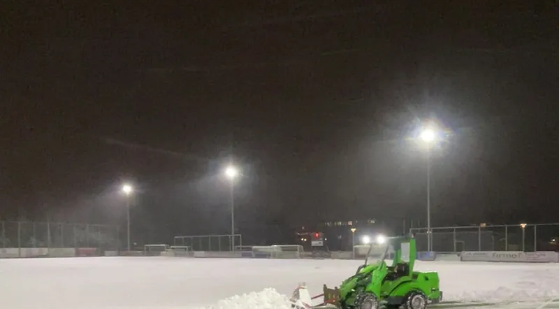 Sneeuwruimen met een sneeuwschuif op een sportveld bij kunstlicht