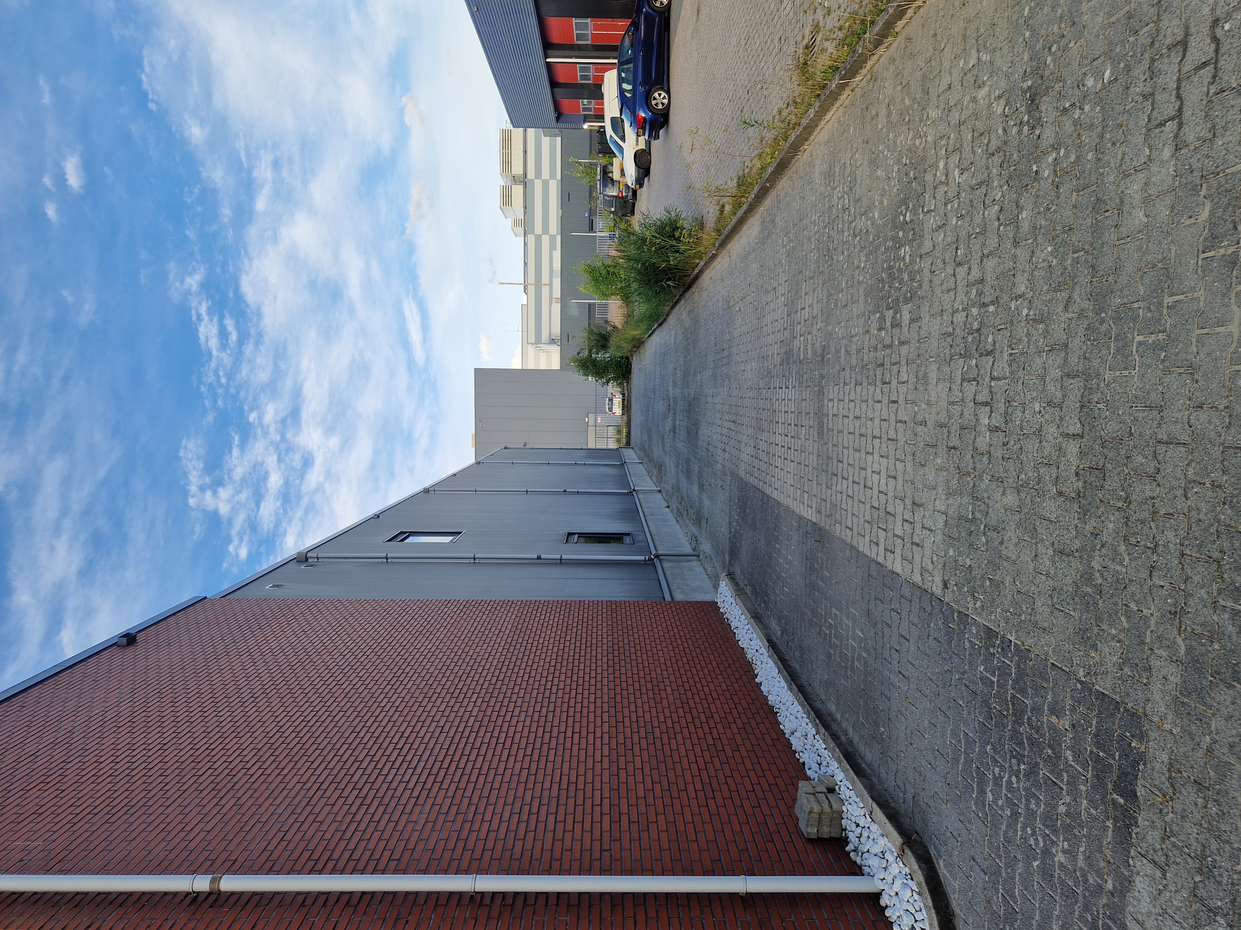 Onderhoud van een bestraat pad langs een bedrijfspand, met zicht op de industriële gevels