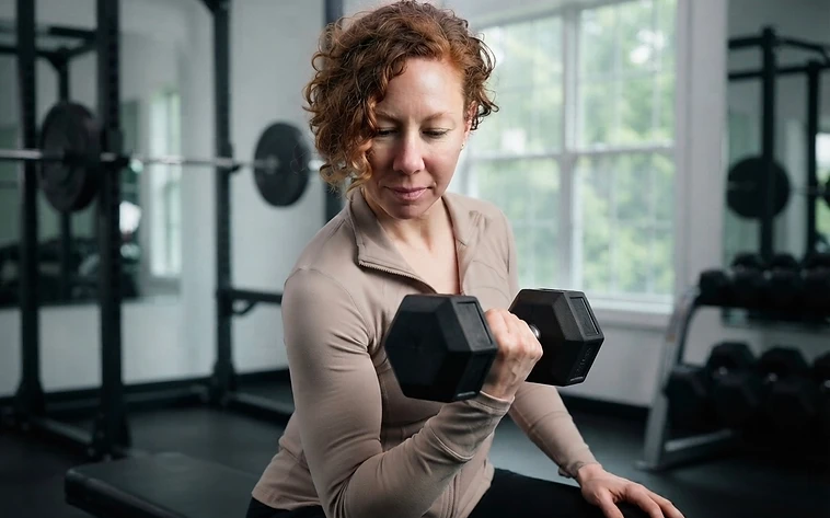 A woman performing a bicep curl with a black dumbbell in a home gym