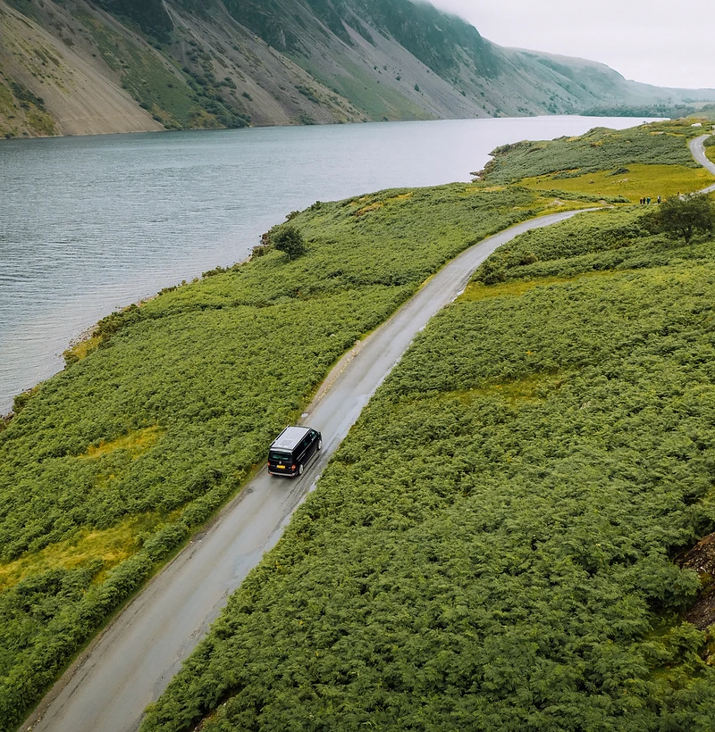 Albatross camper van driving a fern-lined road beside mountain water