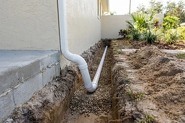 Open trench with PVC drainage pipe connected to a downspout along a Florida foundation