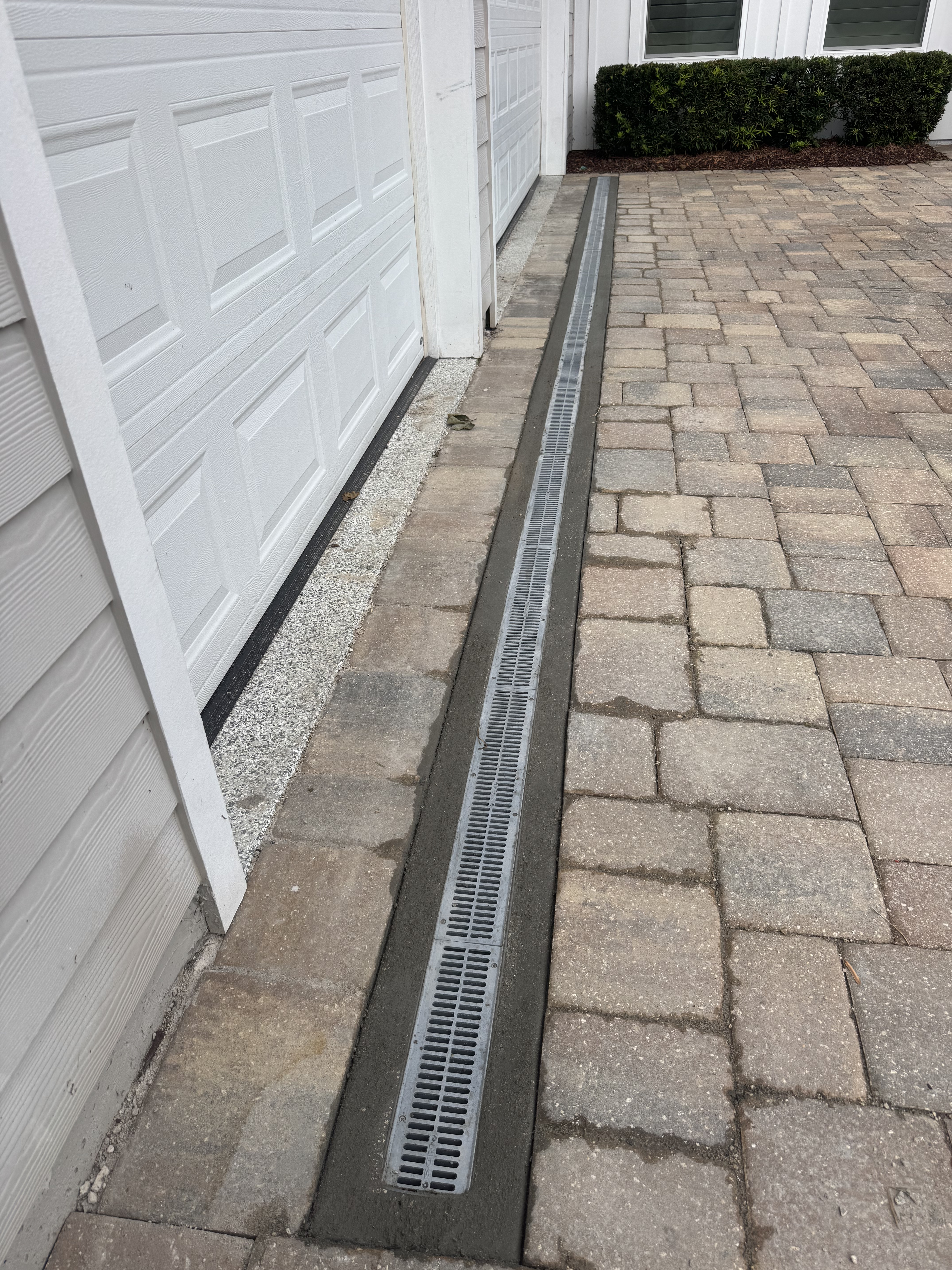 Trench drain set into a paver driveway in front of a garage door