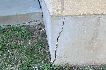 Crack in a stone-and-concrete foundation corner beneath an ungutttered roof edge
