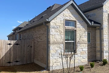 Grey seamless gutters and downspouts on a brick-and-stone home near Austin TX