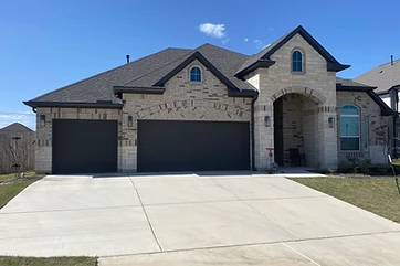 Stone-front Austin-area home with black seamless gutters along every roofline