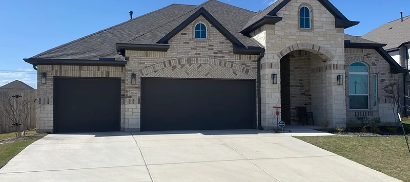 Stone-front Austin-area home with black seamless gutters installed along every roofline