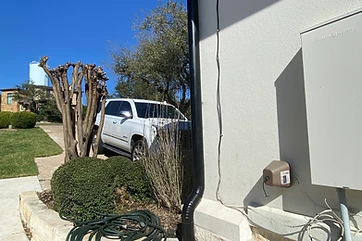Black round downspout carrying roof water down a stucco wall to grade