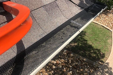 Mesh gutter guard installed over a seamless gutter beneath a shingle roof edge
