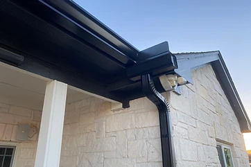 Black mitered gutter corner and downspout at a covered porch on a stone home