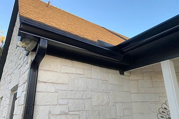 Black seamless gutter and downspout on a white limestone home near Austin TX