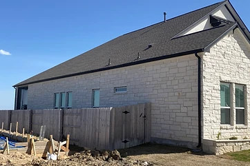 Side elevation of a white stone home with black seamless gutters and downspouts