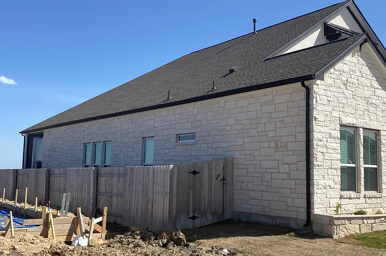 Seamless gutters and a downspout installed along the side of a stone home near Austin TX