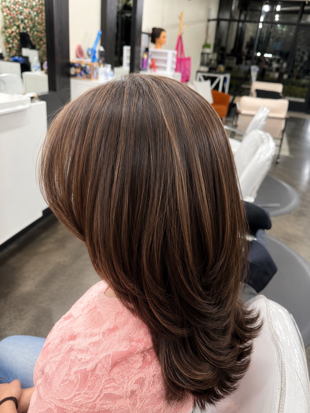 Long layered chestnut hair with caramel highlights styled in soft volume