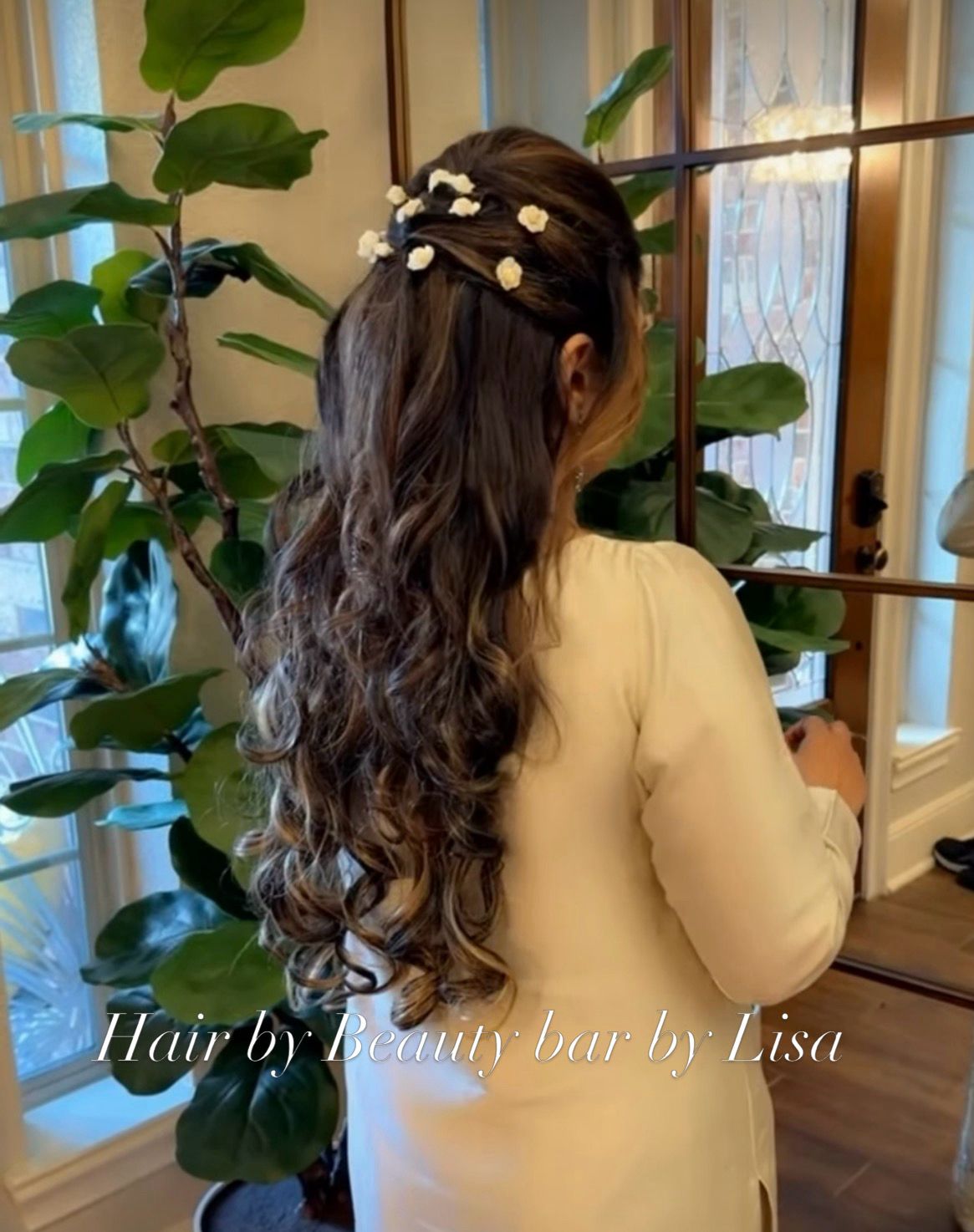 Long dark brown hair in soft voluminous curls pinned half-up with white flowers