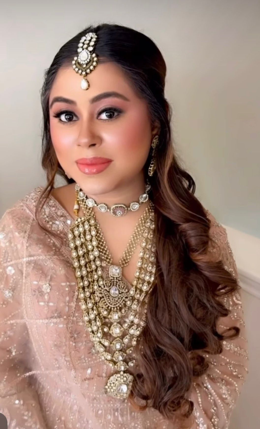 Bridal half-up wavy style with maang tikka and a statement stone necklace