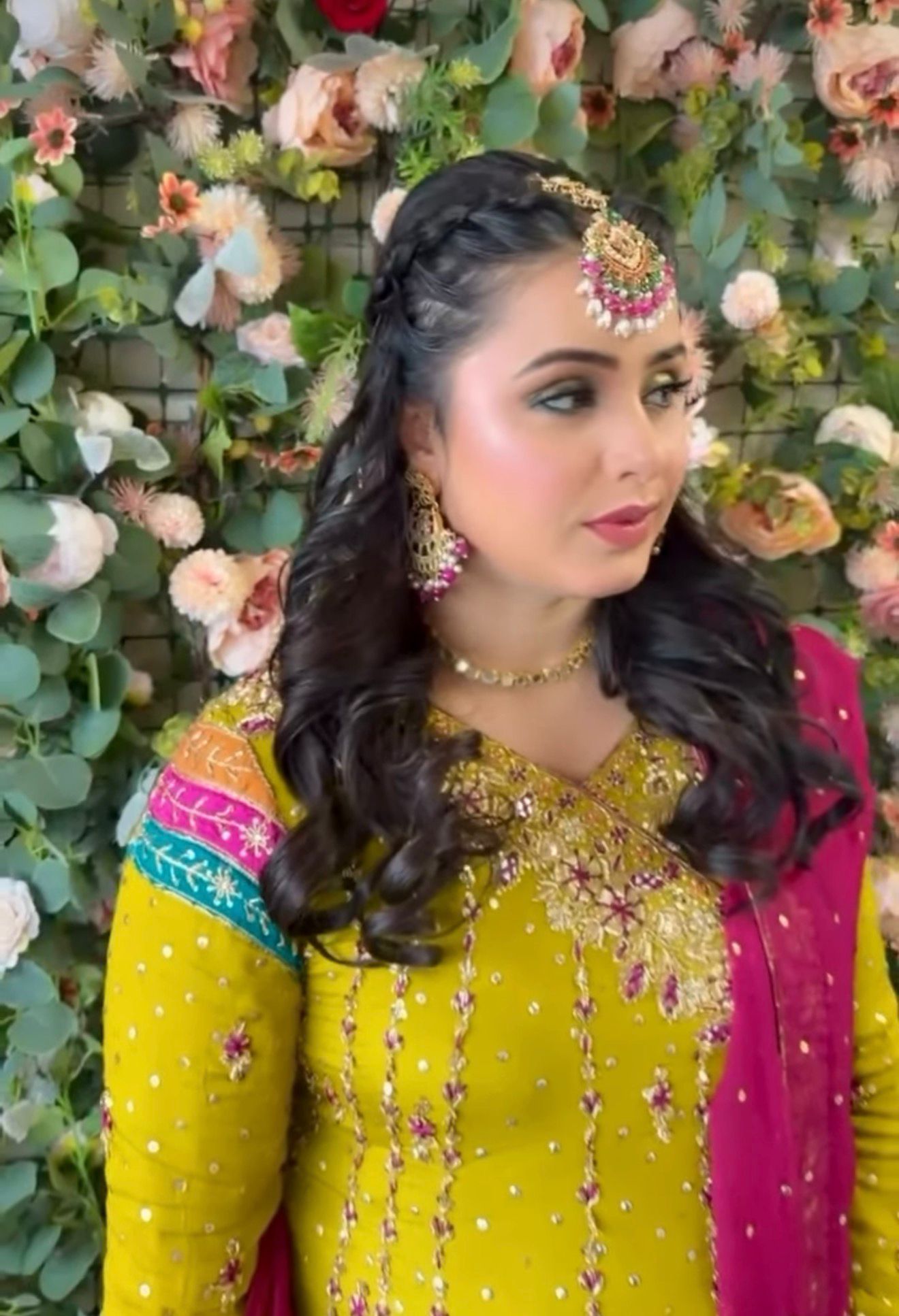 Half-up style with a side braid and traditional headpiece against a floral wall