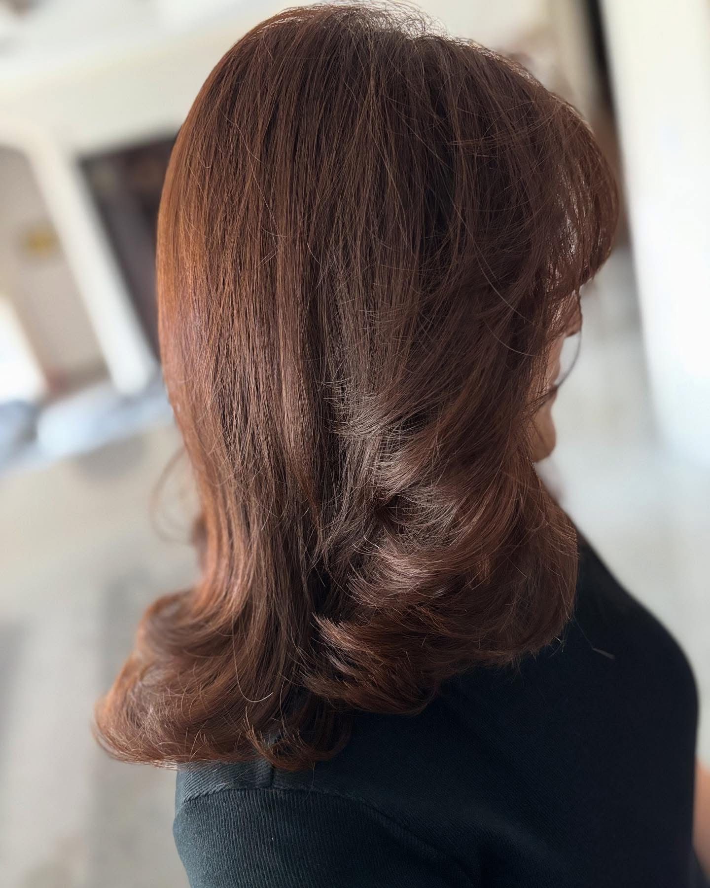 Shoulder-length chestnut-brown hair styled with soft curls flipping out at the ends
