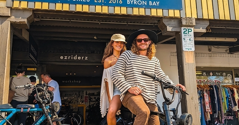 Ezriderz electric bike hire storefront in Byron Bay with riders on a dual-seat e-bike