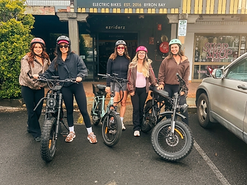 Group of five women with helmets posing on hired e-bikes outside the Ezriderz electric bike shop in Byron Bay