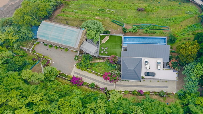 Aerial drone view of the retreat, the pool, recreational hall and main house gathered in a forest clearing above Subathu