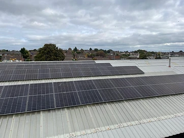 Two banks of black solar panels fitted to a light-grey corrugated metal commercial roof seen from above