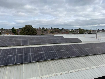 Two banks of black solar panels fitted to a light-grey corrugated metal commercial roof seen from above