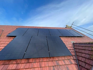 Black monocrystalline solar panels mounted in an L-shaped array on a terracotta-tiled residential roof under a clear blue sky