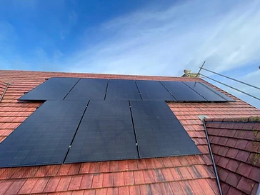 Black monocrystalline solar panels mounted in an L-shaped array on a terracotta-tiled residential roof under a clear blue sky