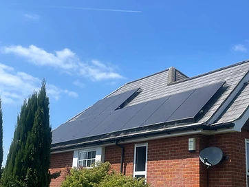 Black solar panels installed on a grey slate-tiled roof above a red brick wall with a clear blue sky