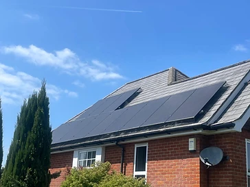 Black solar panels installed on a grey slate-tiled roof above a red brick wall with a clear blue sky